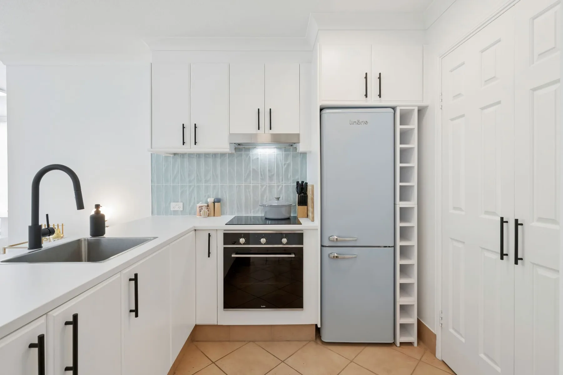 Una cocina blanca y luminosa, con electrodomésticos integrados y azulejos azul claro.