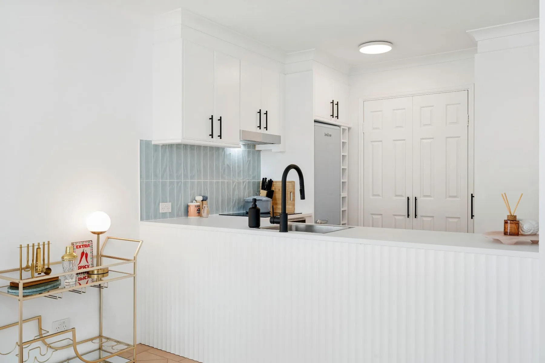 Una cocina luminosa con gabinetes blancos, un salpicadero de azulejos y una encimera.