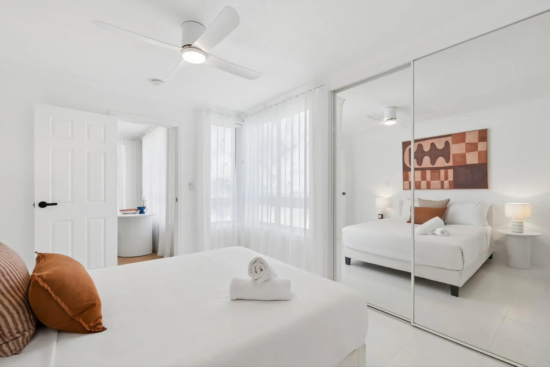 Un dormitorio luminoso con ropa de cama blanca y puertas de armario espejadas.