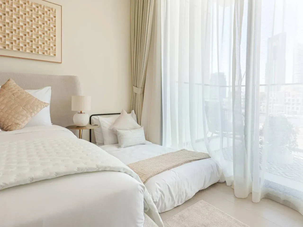 A bright bedroom with two beds beside a large curtained window.