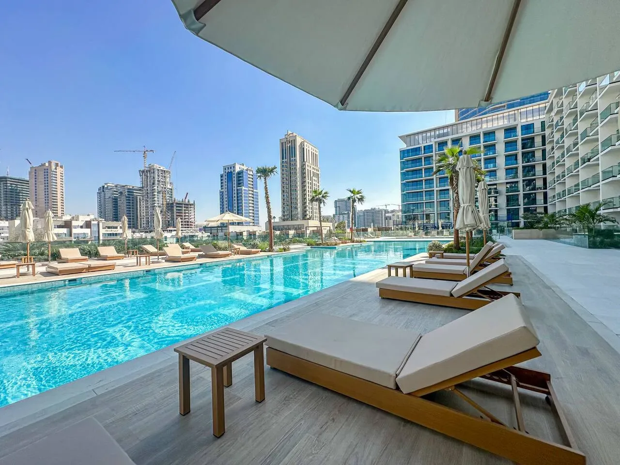 A rooftop pool with loungers overlooks a city skyline.