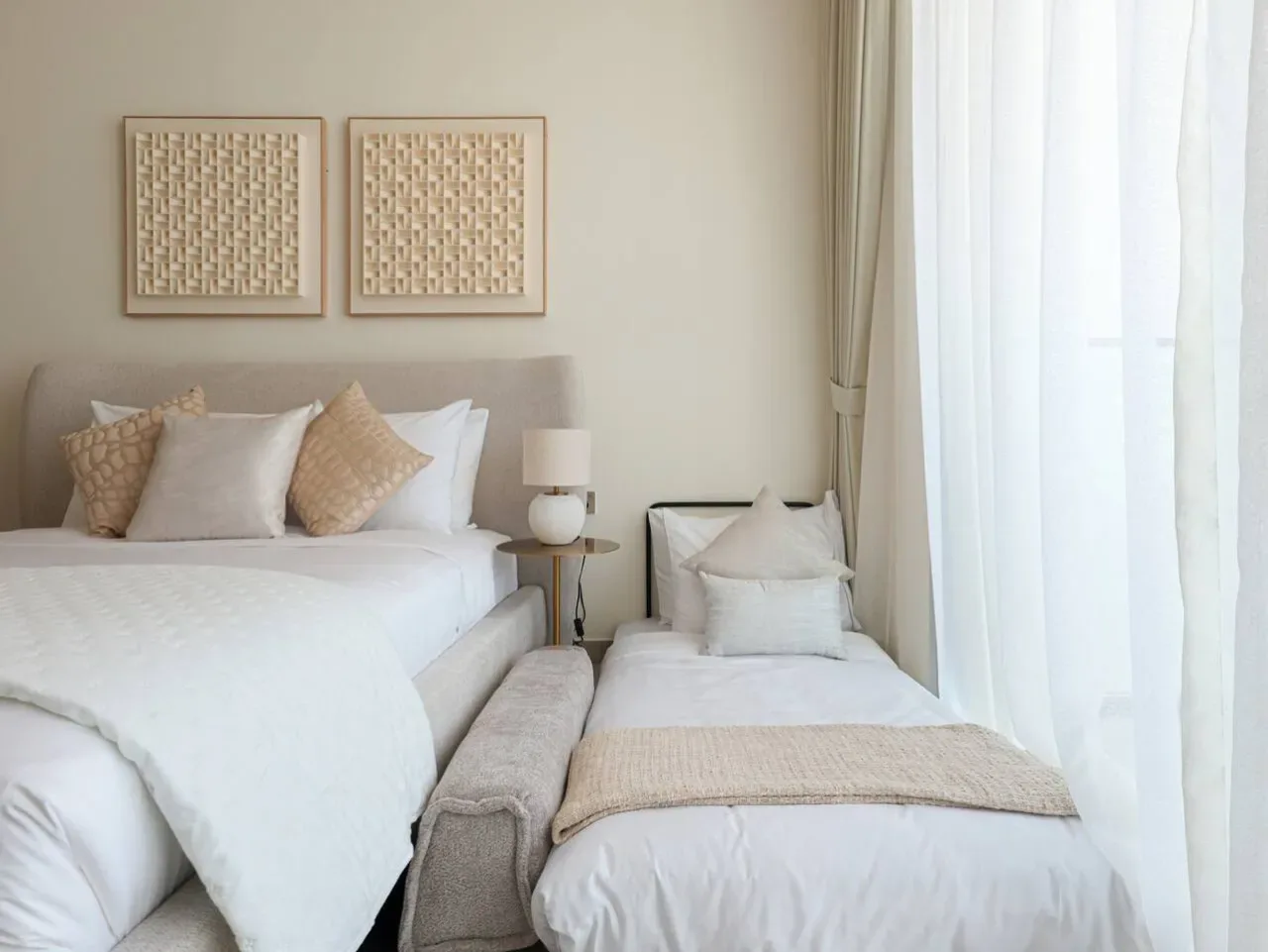A bright bedroom with a large bed and a smaller bed beside the window.