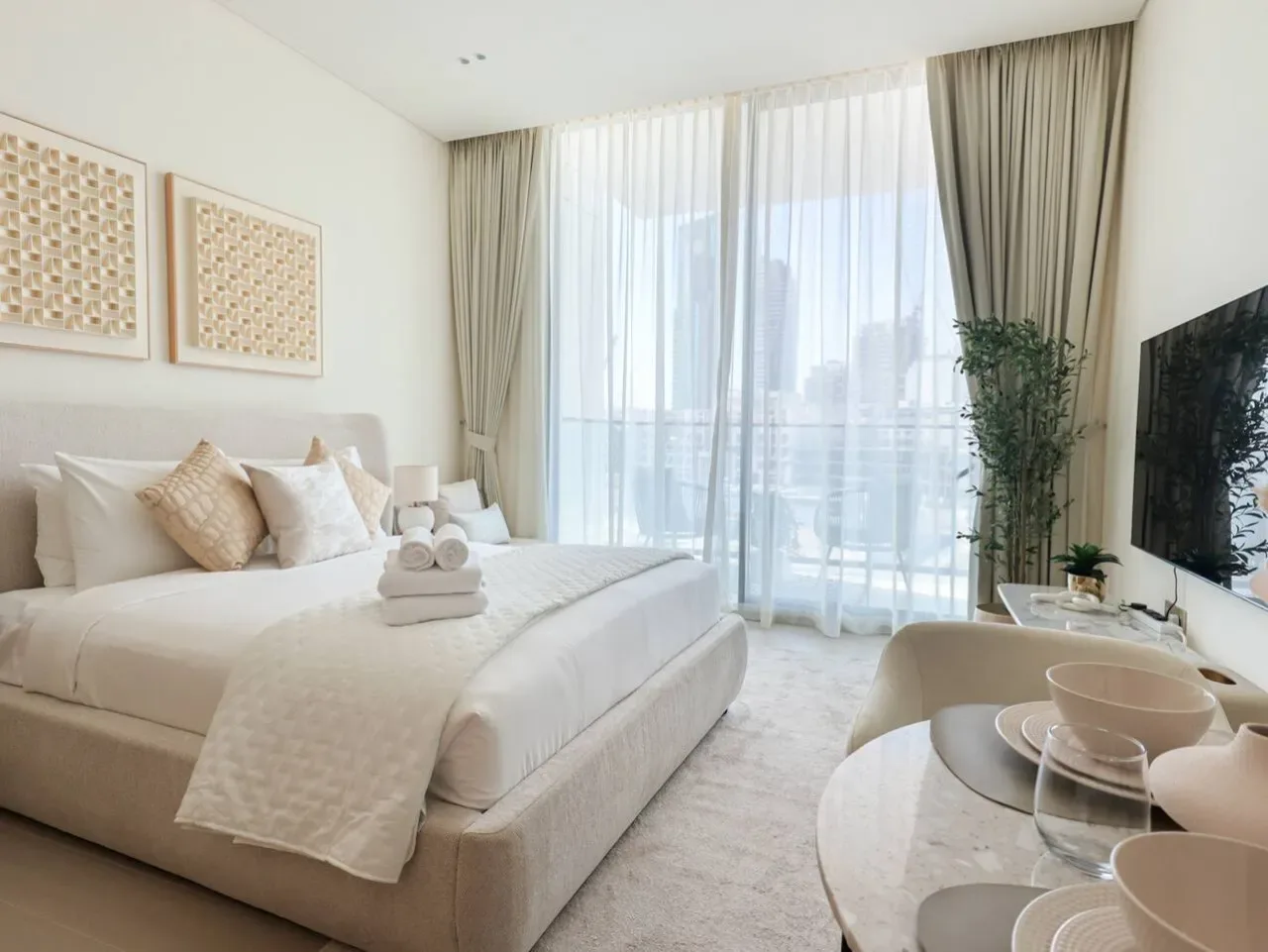 A bright bedroom with a neatly made bed beside a large curtained window.