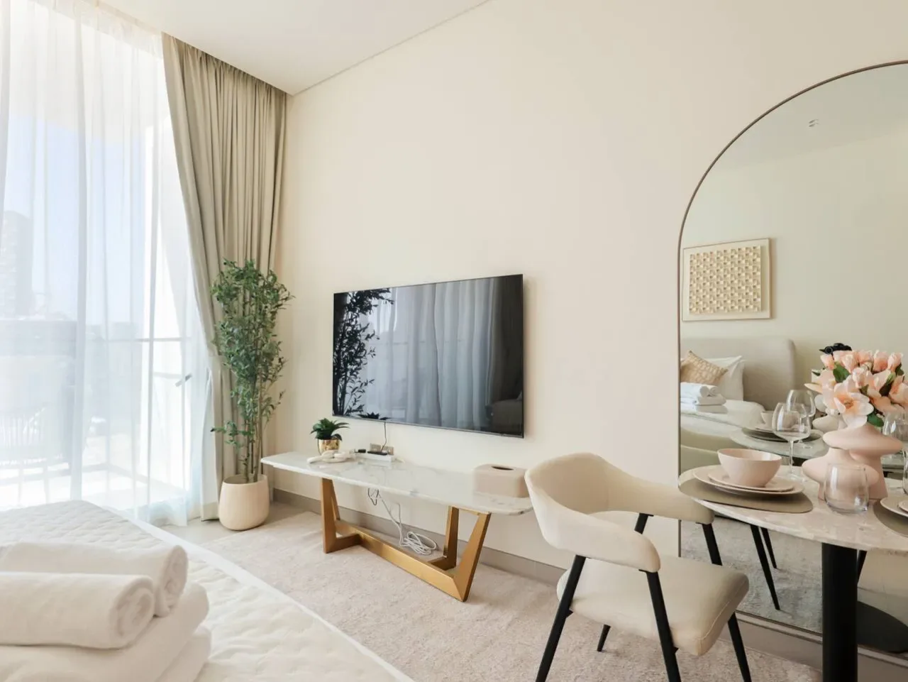 A bright living and dining area with a television, seating, and a large window.