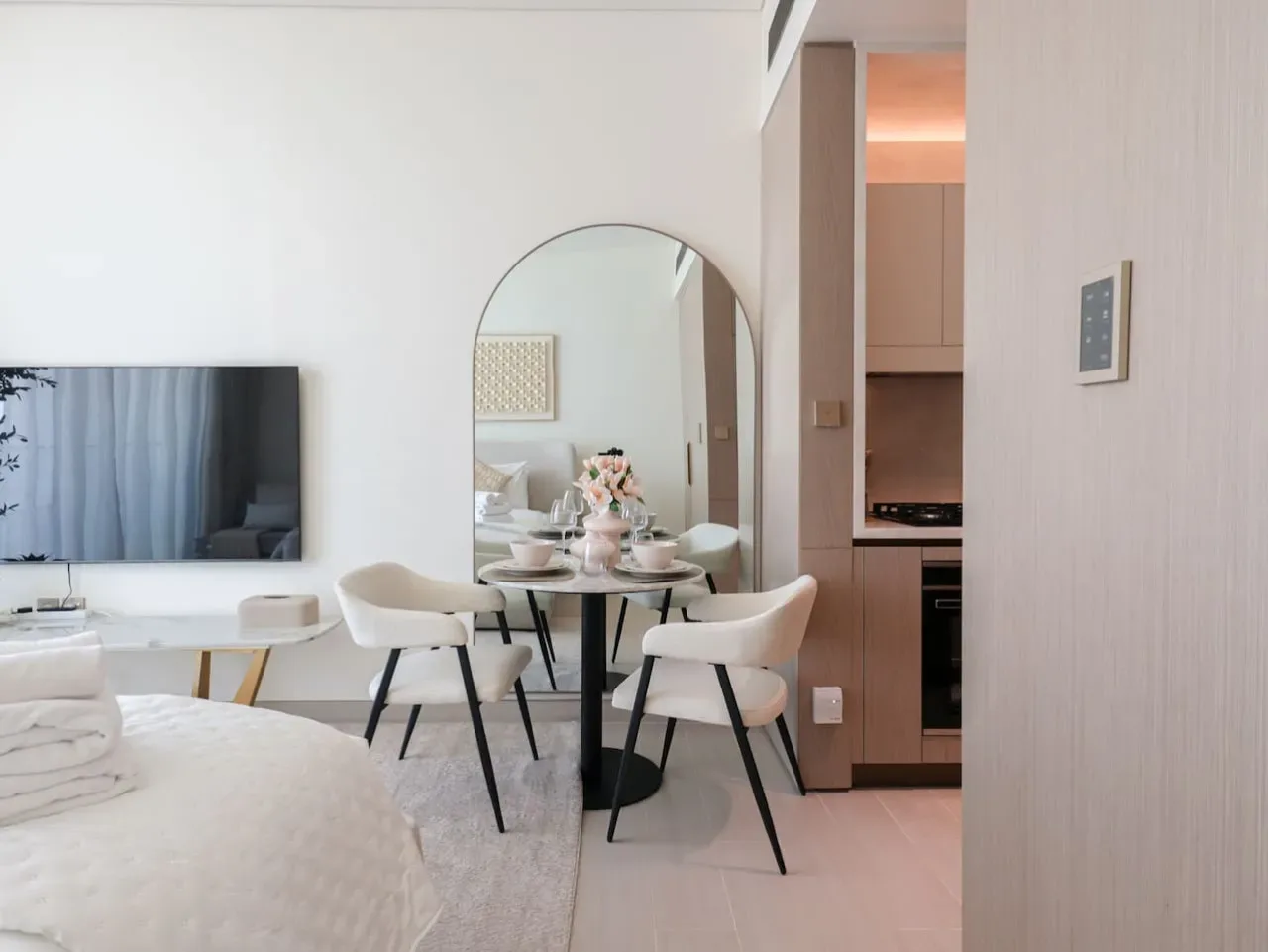 A bright open-plan room combines a sleeping area, dining table, and compact kitchen.