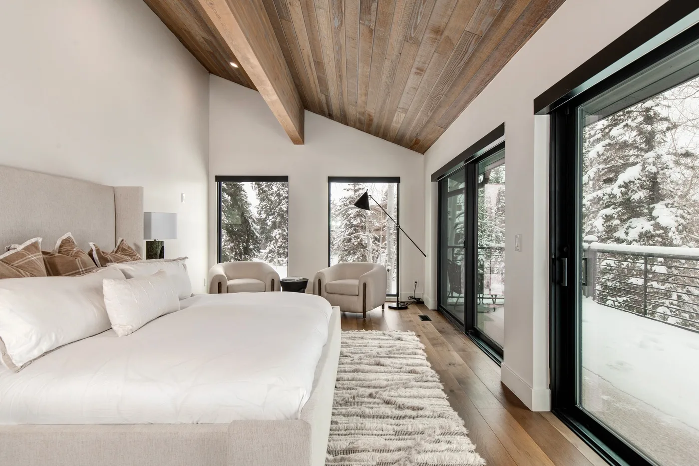Un dormitorio luminoso tiene una cama grande y ventanas con vistas a un paisaje nevado.