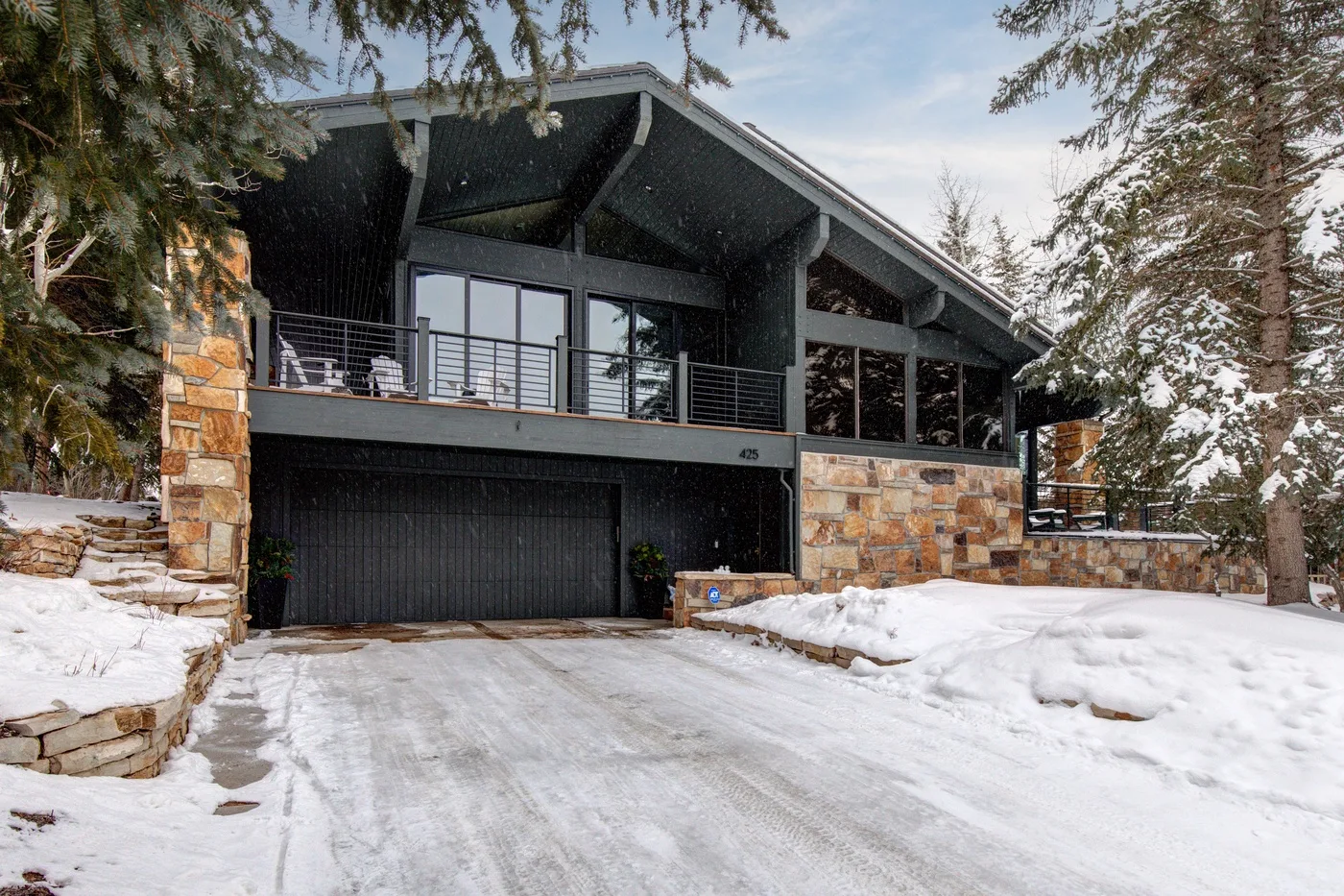Una casa moderna con una amplia entrada de garaje está junto a un camino cubierto de nieve.