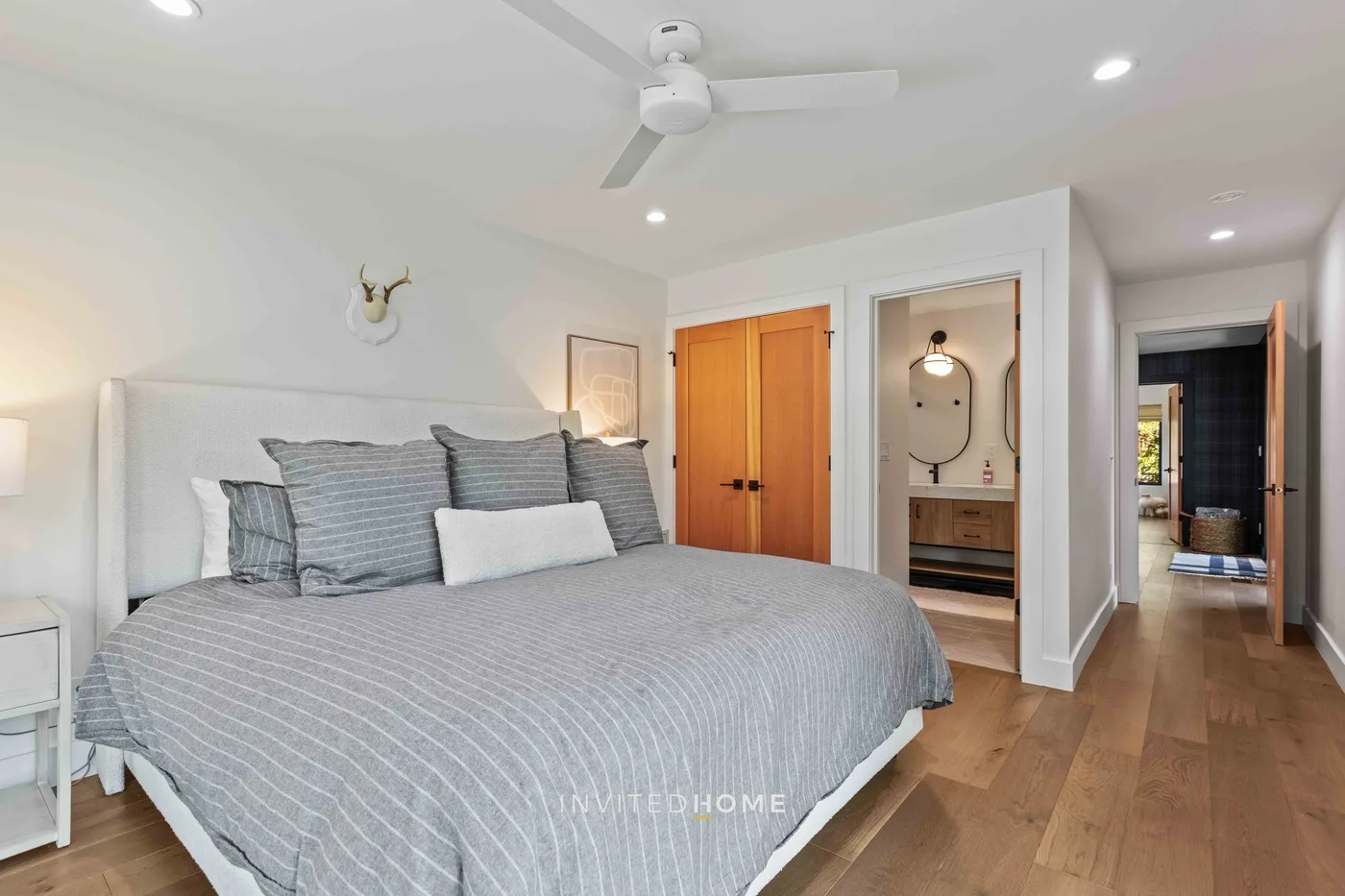 Un dormitorio luminoso con una cama grande, ventilador de techo y puertas de madera.