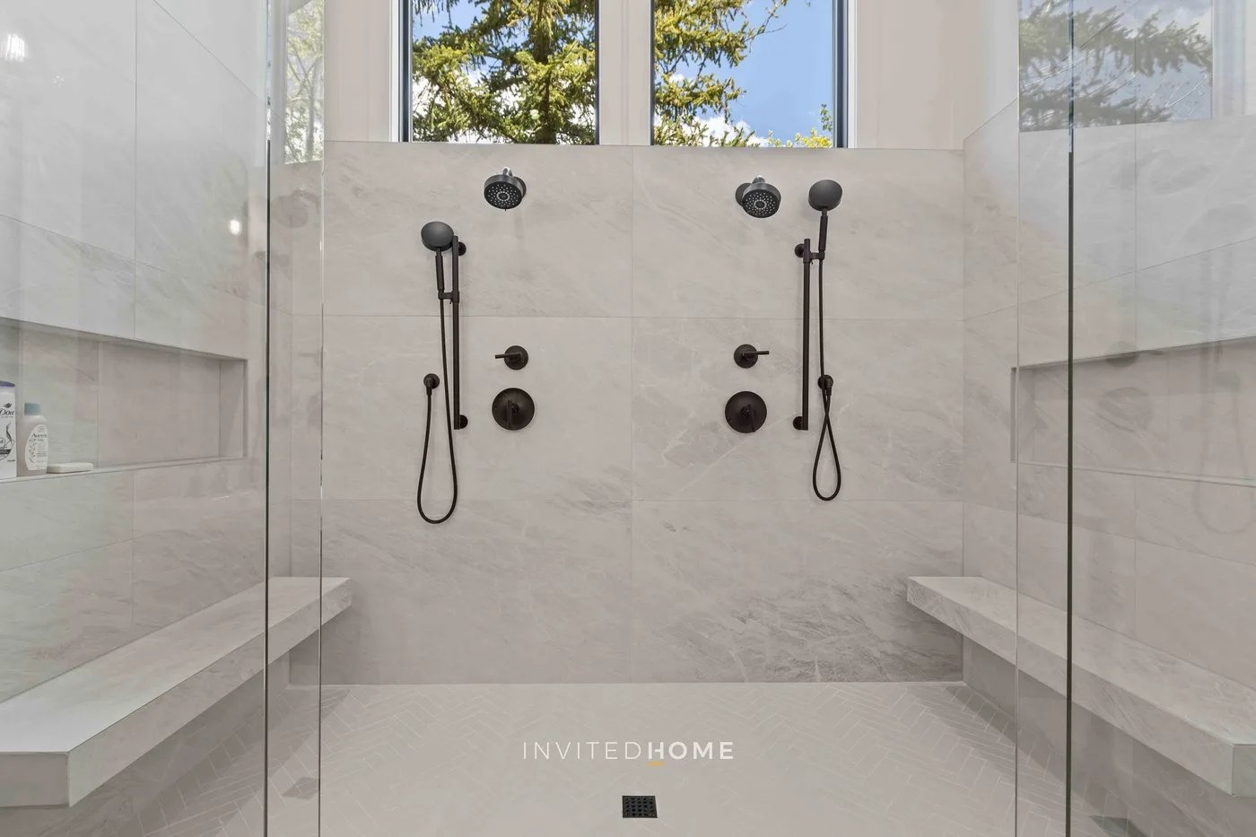 Un baño de ducha luminoso con paneles de vidrio y ventanas que dan a los árboles.