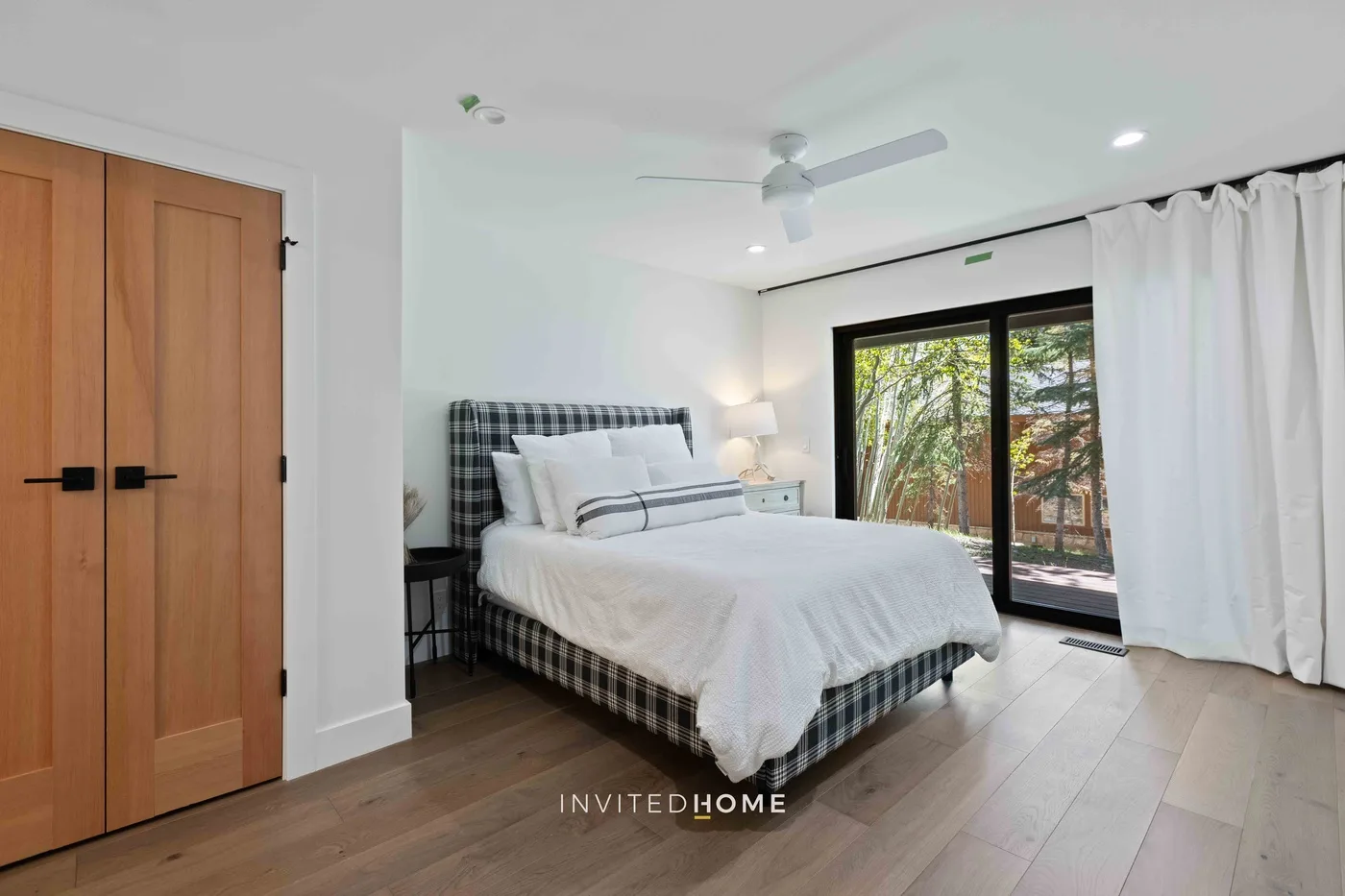 Un dormitorio luminoso con una cama bien tendida y puertas corredizas de vidrio hacia la vegetación.