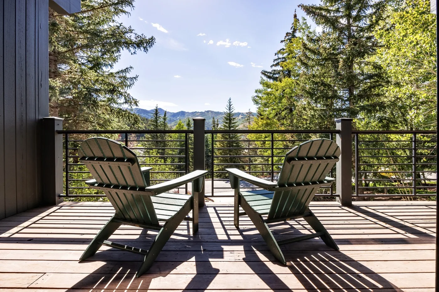 Una terraza de madera con dos sillas de exterior da a árboles y colinas lejanas.