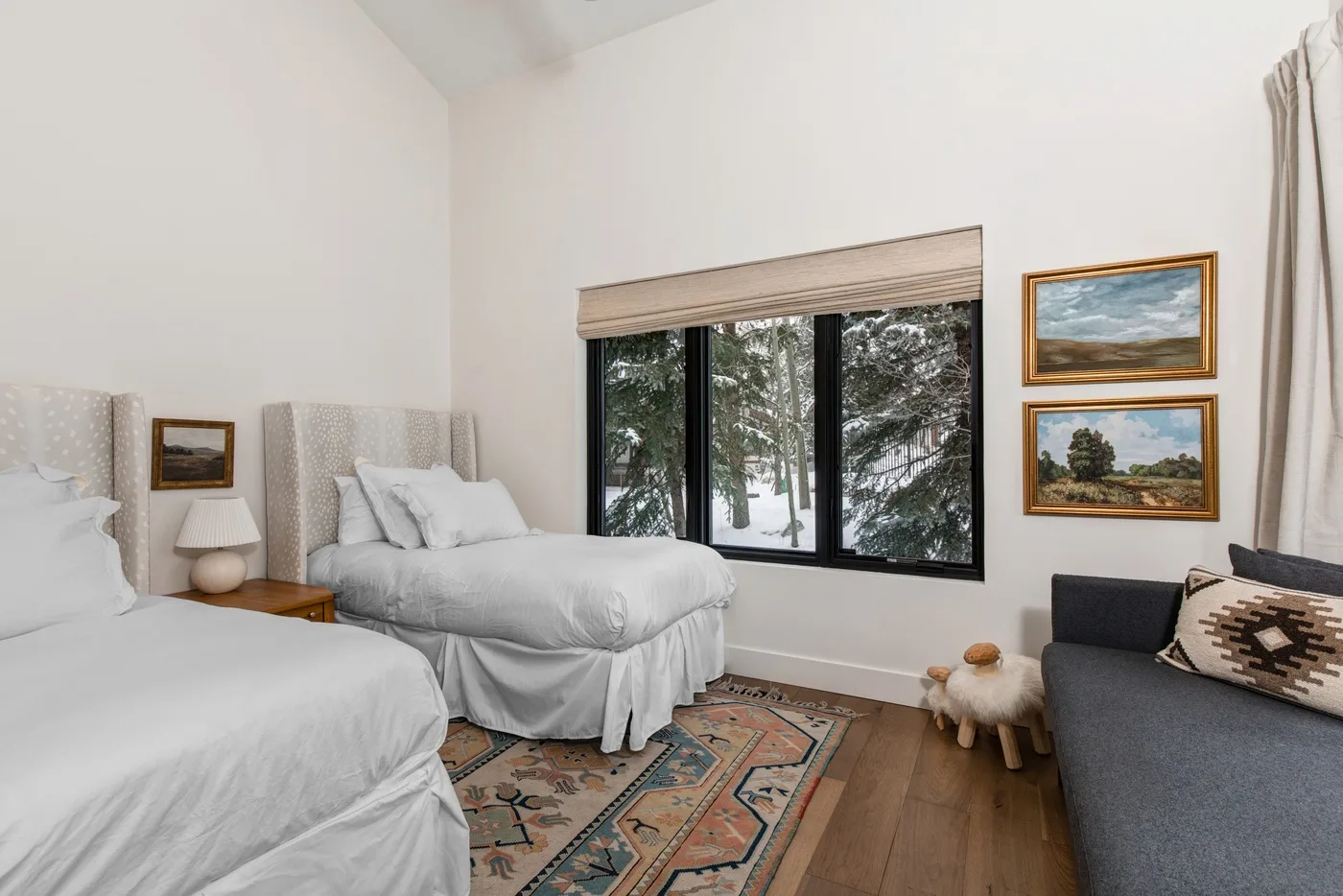 Un dormitorio luminoso con dos camas, una alfombra estampada y una ventana grande.