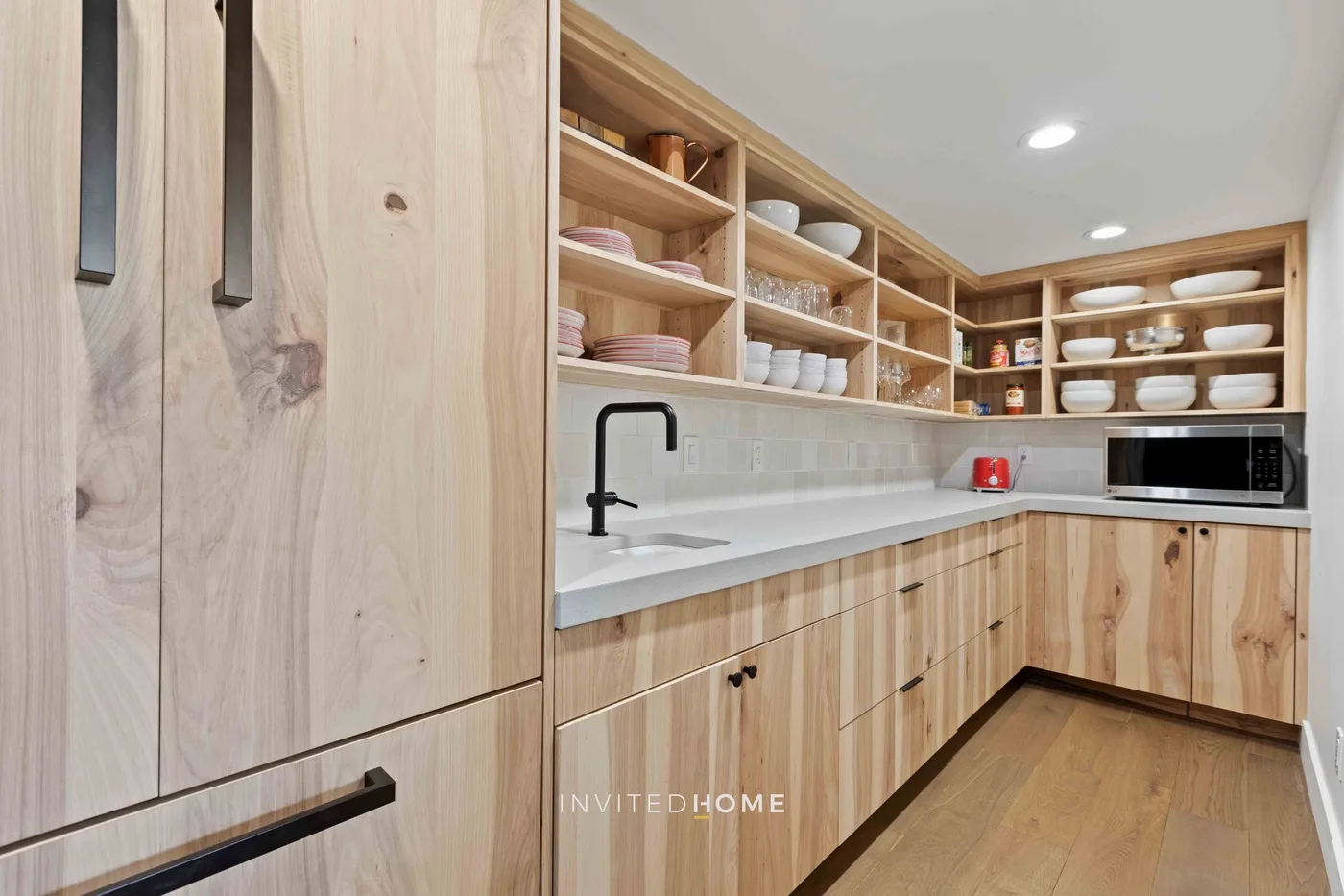 Una cocina con gabinetes de madera clara, estantes abiertos y una encimera larga.