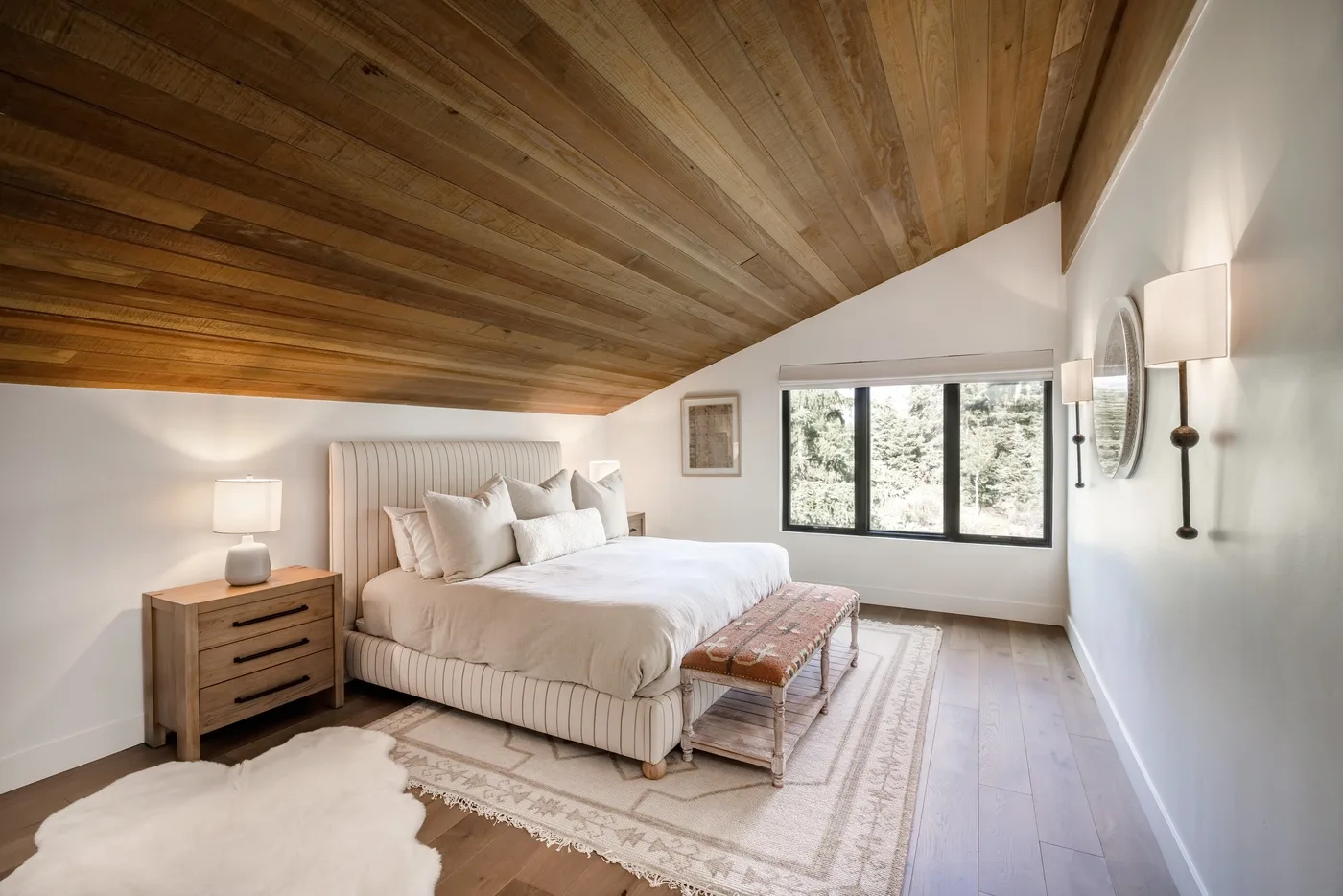 Un dormitorio luminoso con una cama bajo un techo inclinado de madera y ventanas.