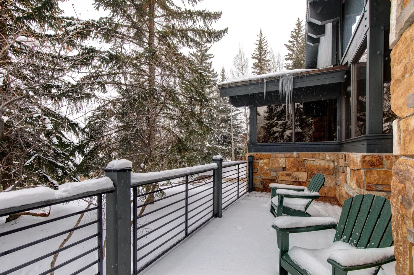 Una terraza exterior cubierta de nieve junto a un edificio, con asientos y una barandilla metálica.
