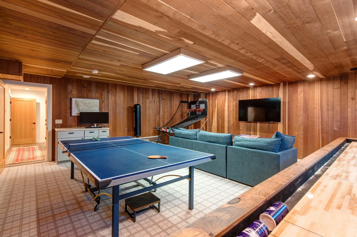 Una sala de juegos con paredes de madera, mesa de ping-pong, asientos y mesa de billar.