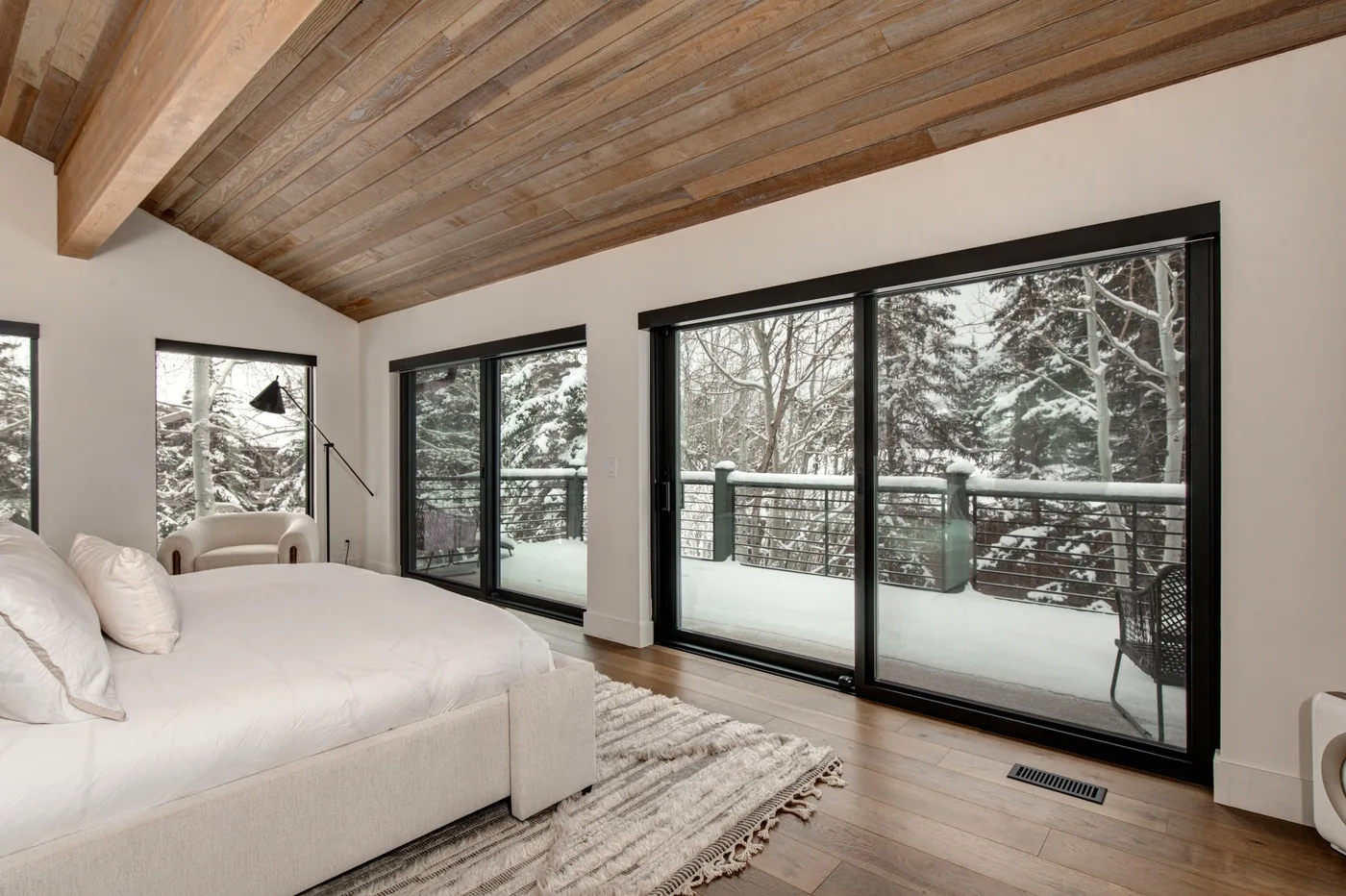 Un dormitorio luminoso con una cama junto a grandes ventanales que dan a un paisaje nevado.