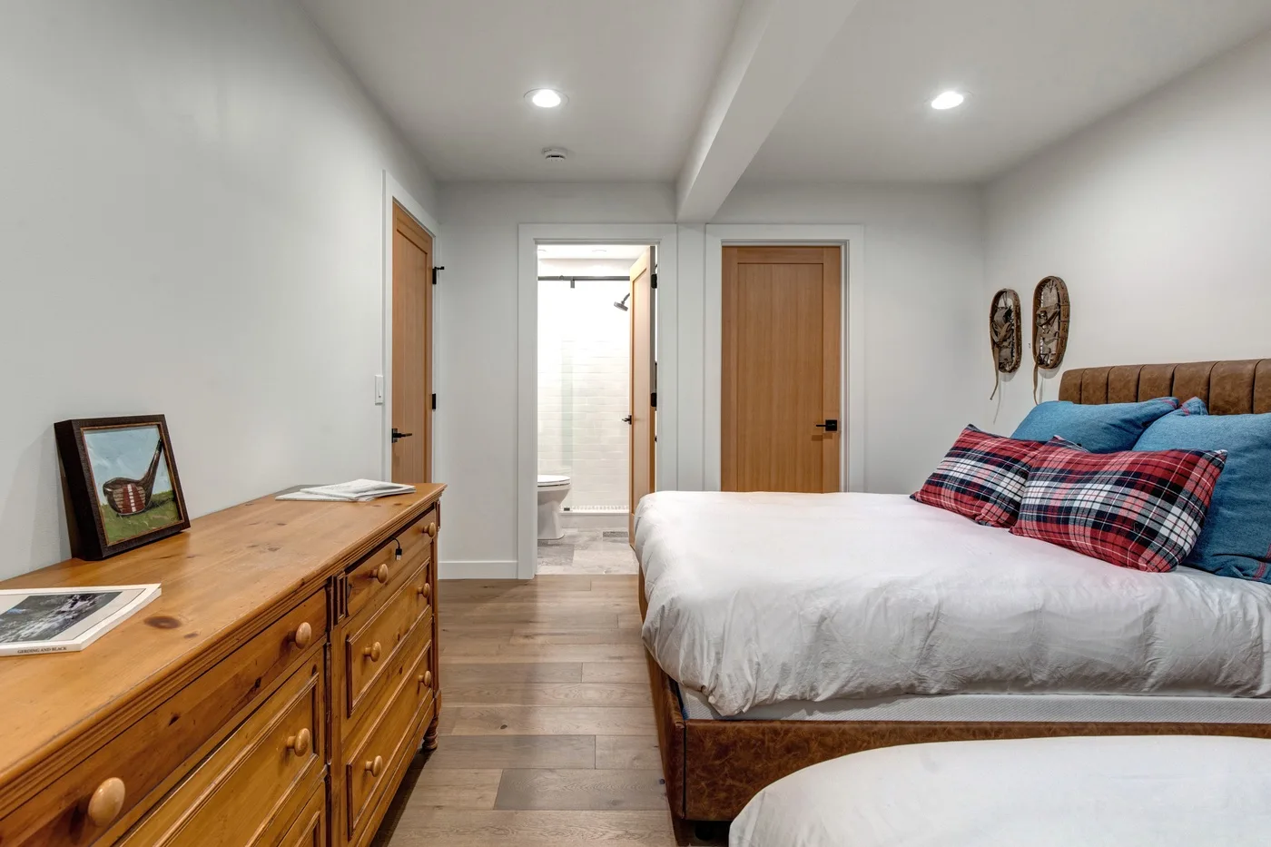 Un dormitorio con una cómoda de madera, una cama y una entrada a un baño iluminado.
