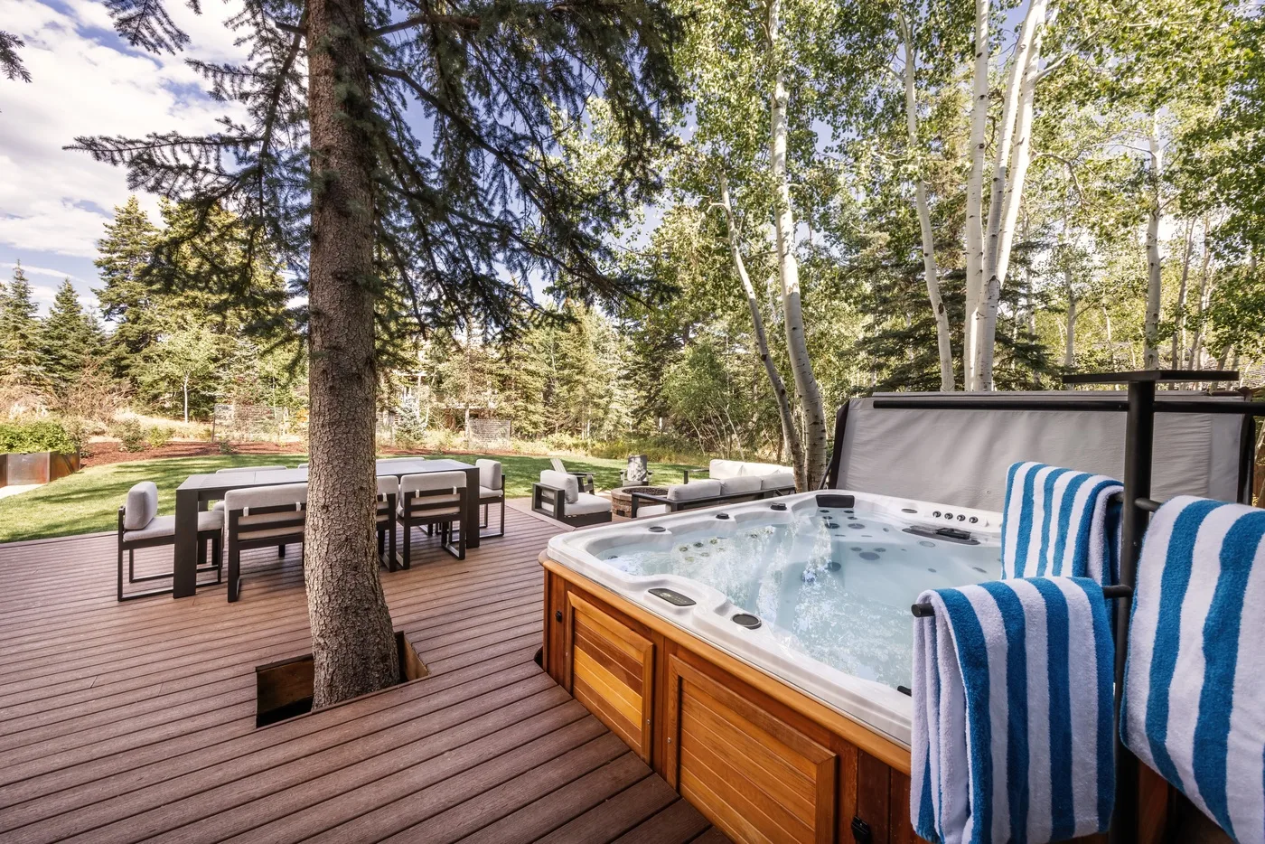 Una terraza exterior con una bañera de hidromasaje y una mesa de comedor entre árboles.