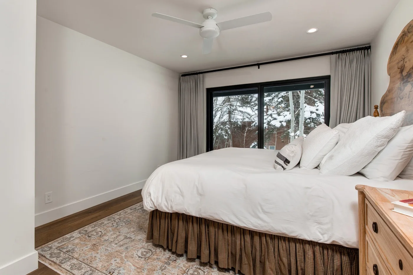Un dormitorio luminoso con una cama bien tendida y una gran ventana con vistas a los árboles.
