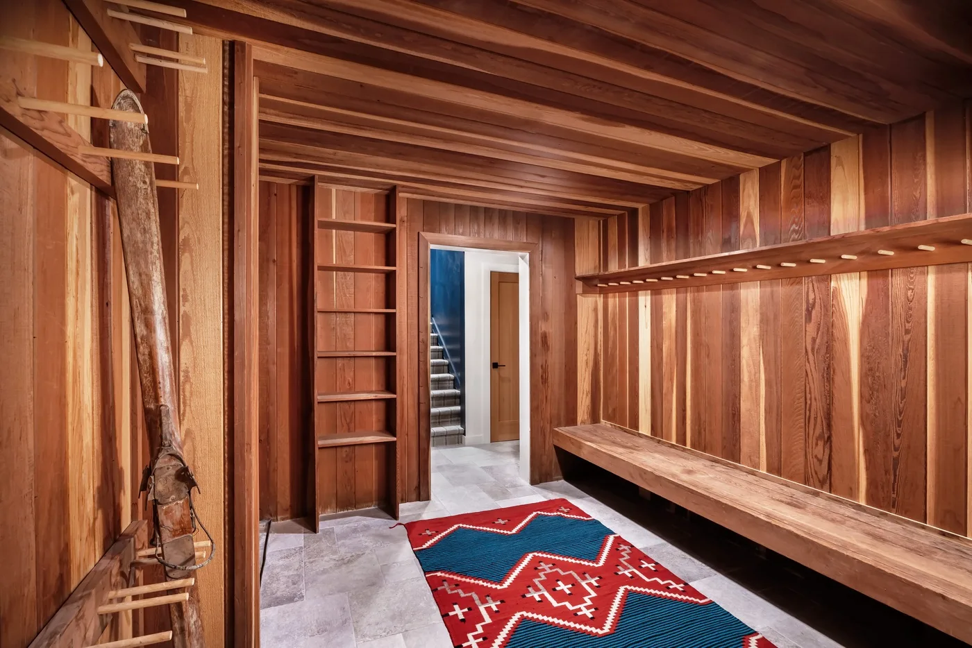 Una habitación revestida de madera con un banco largo y una alfombra estampada de colores.