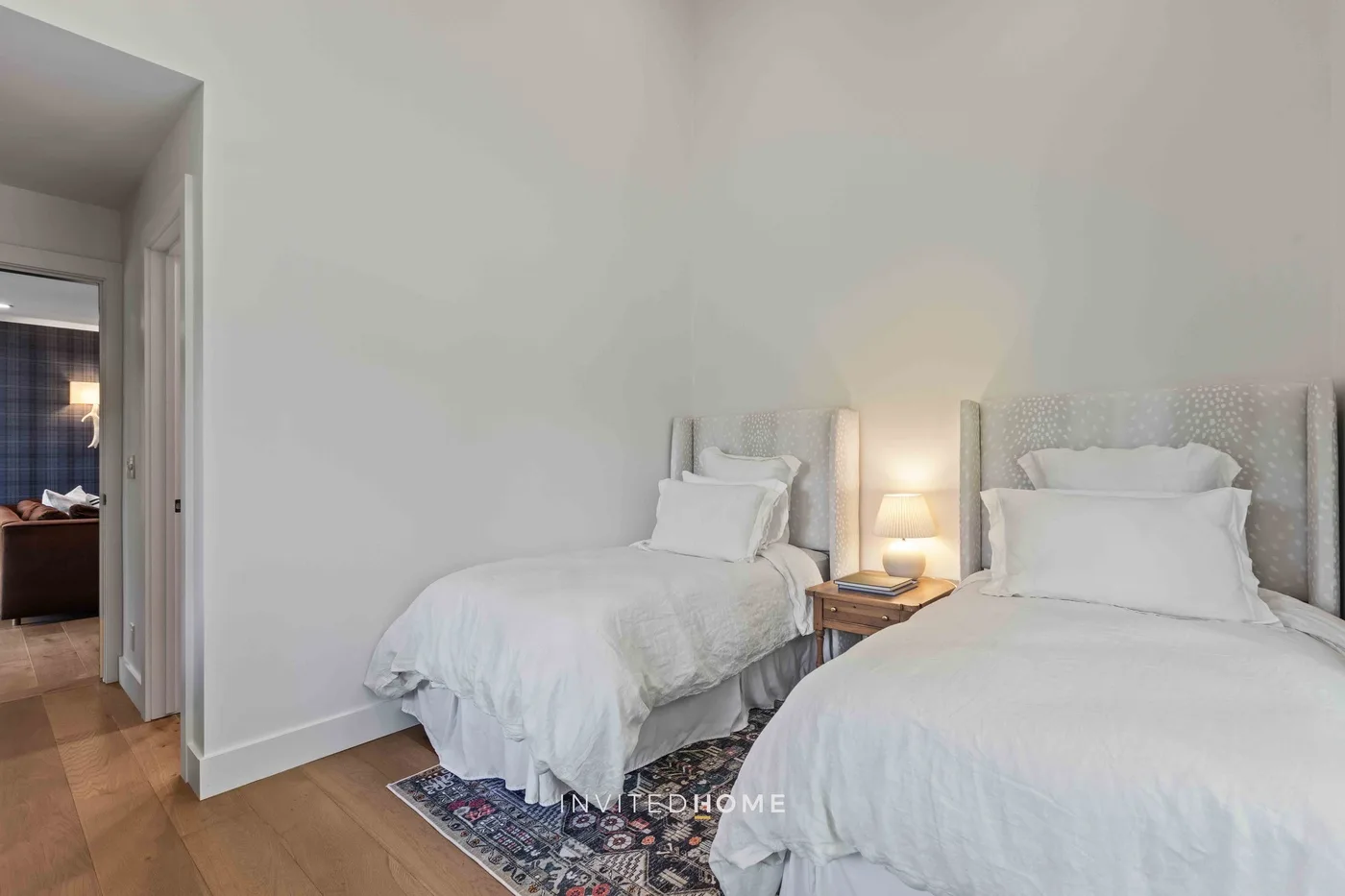 Un dormitorio luminoso con dos camas, ropa de cama blanca y una mesita de noche.