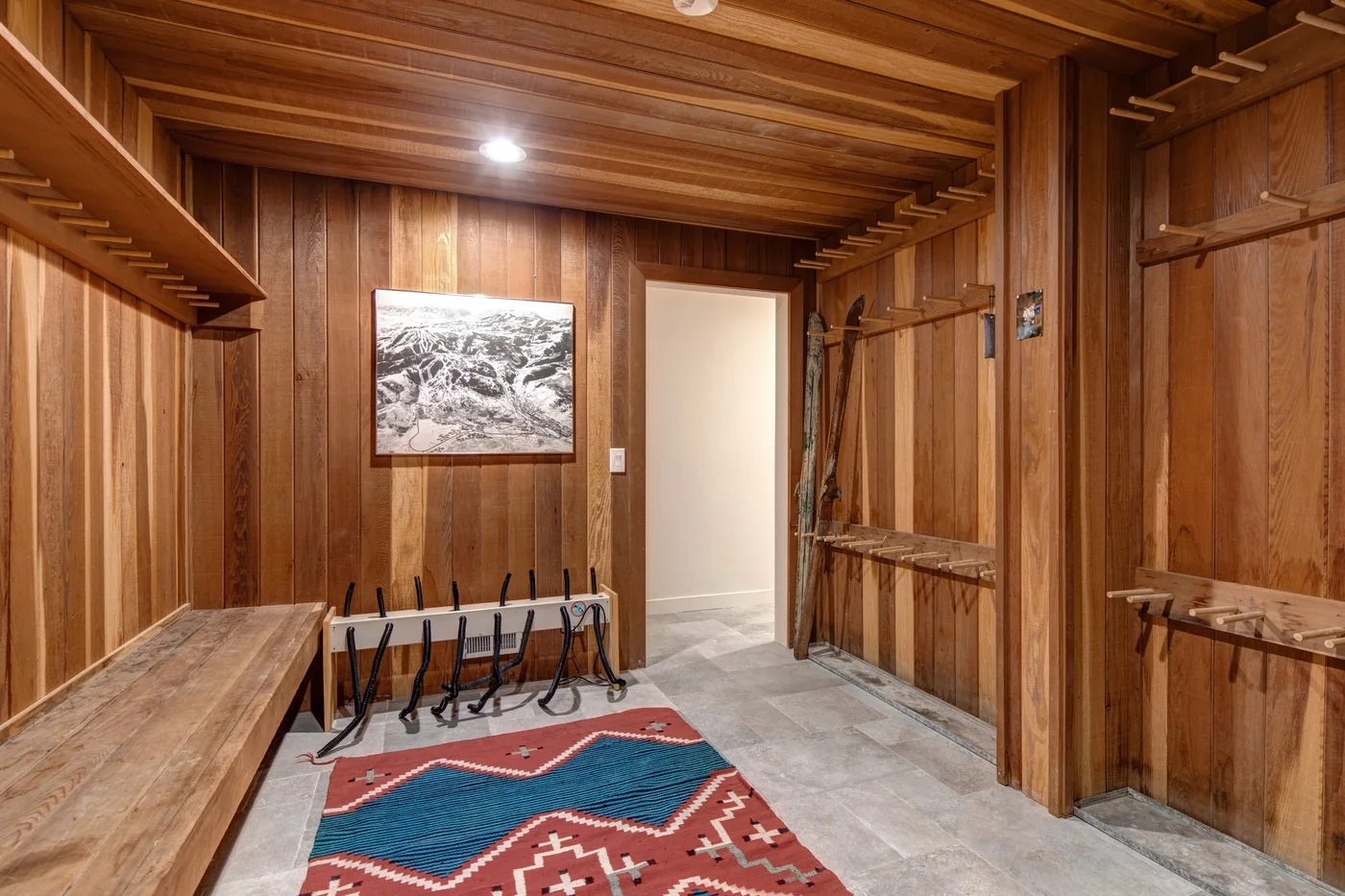 Un cuarto de almacenamiento de esquís con paredes de madera tiene soportes para equipo y una alfombra estampada.