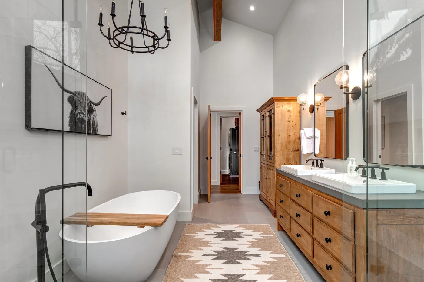 Un baño amplio cuenta con una bañera exenta, un largo mueble de madera y una alfombra estampada.