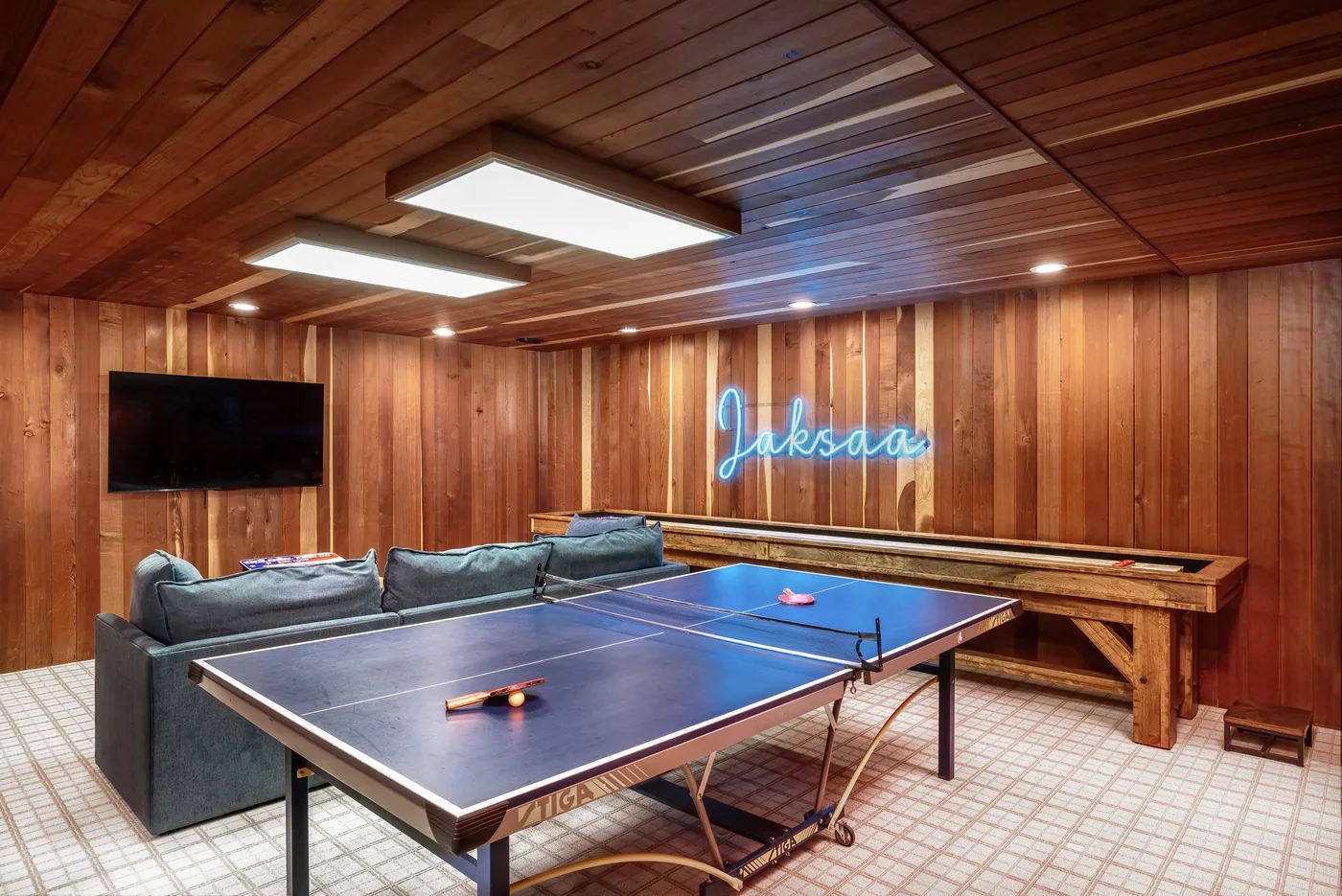 Una sala de juegos revestida de madera tiene una mesa de ping-pong y asientos.