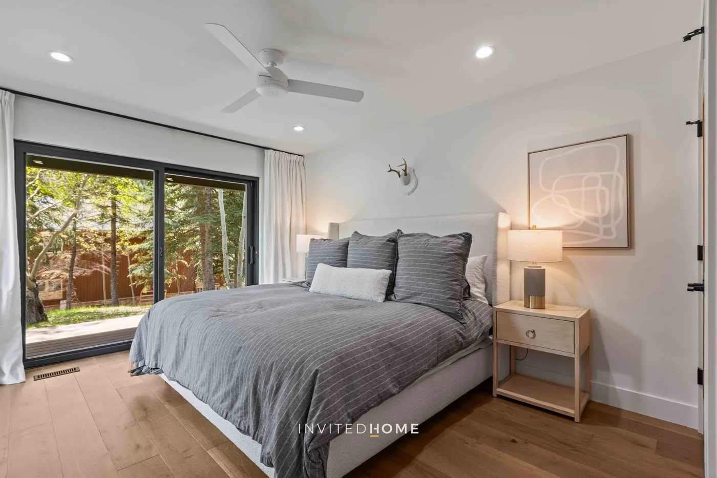 Un dormitorio con una cama tendida junto a grandes ventanas con vistas a la vegetación.
