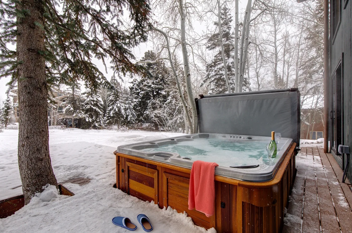 Una bañera de hidromasaje al aire libre está junto a una zona boscosa nevada.