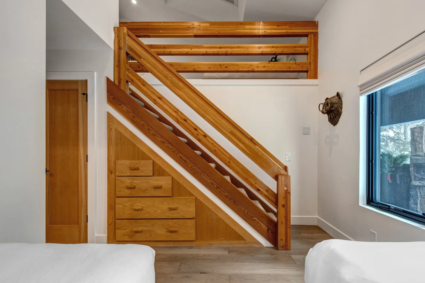 Un dormitorio luminoso con una escalera de madera y cajones empotrados debajo.