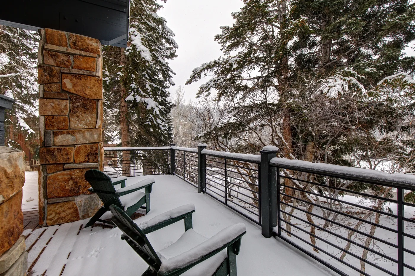 Una terraza exterior cubierta de nieve con asientos da a un paisaje boscoso.
