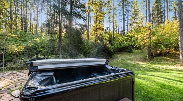 Una bañera de hidromasaje al aire libre está junto a un claro cubierto de césped y rodeado de árboles.