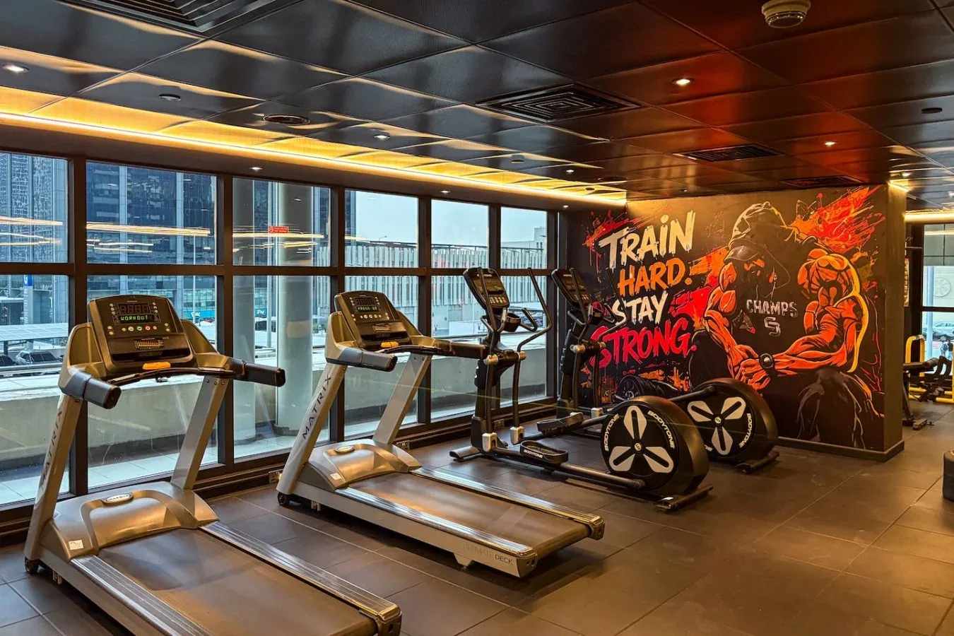 Un gimnasio con cintas de correr y bicicletas estáticas junto a un mural colorido.