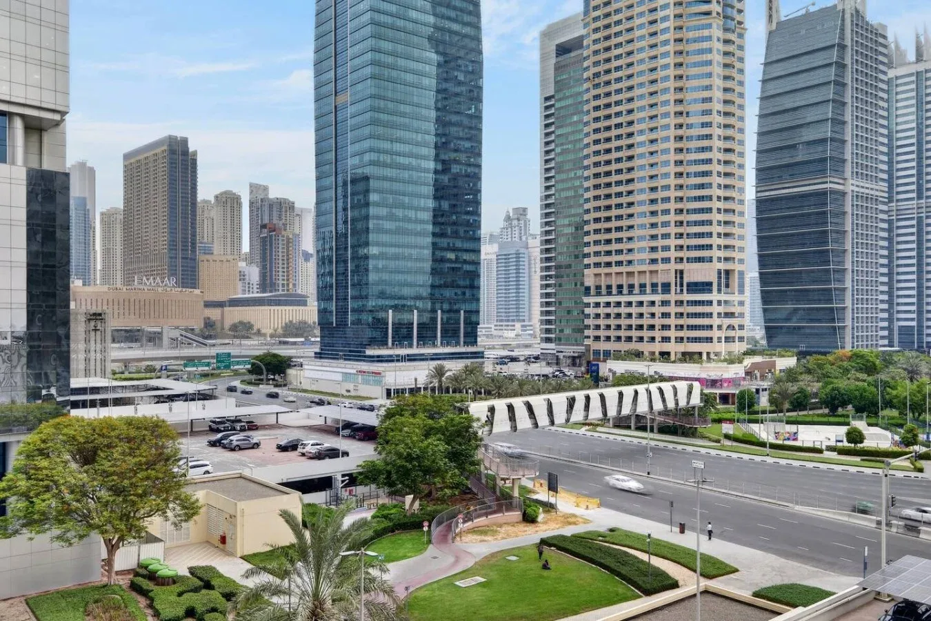 Un paisaje urbano de altas torres de oficinas se alza sobre jardines y una amplia avenida.
