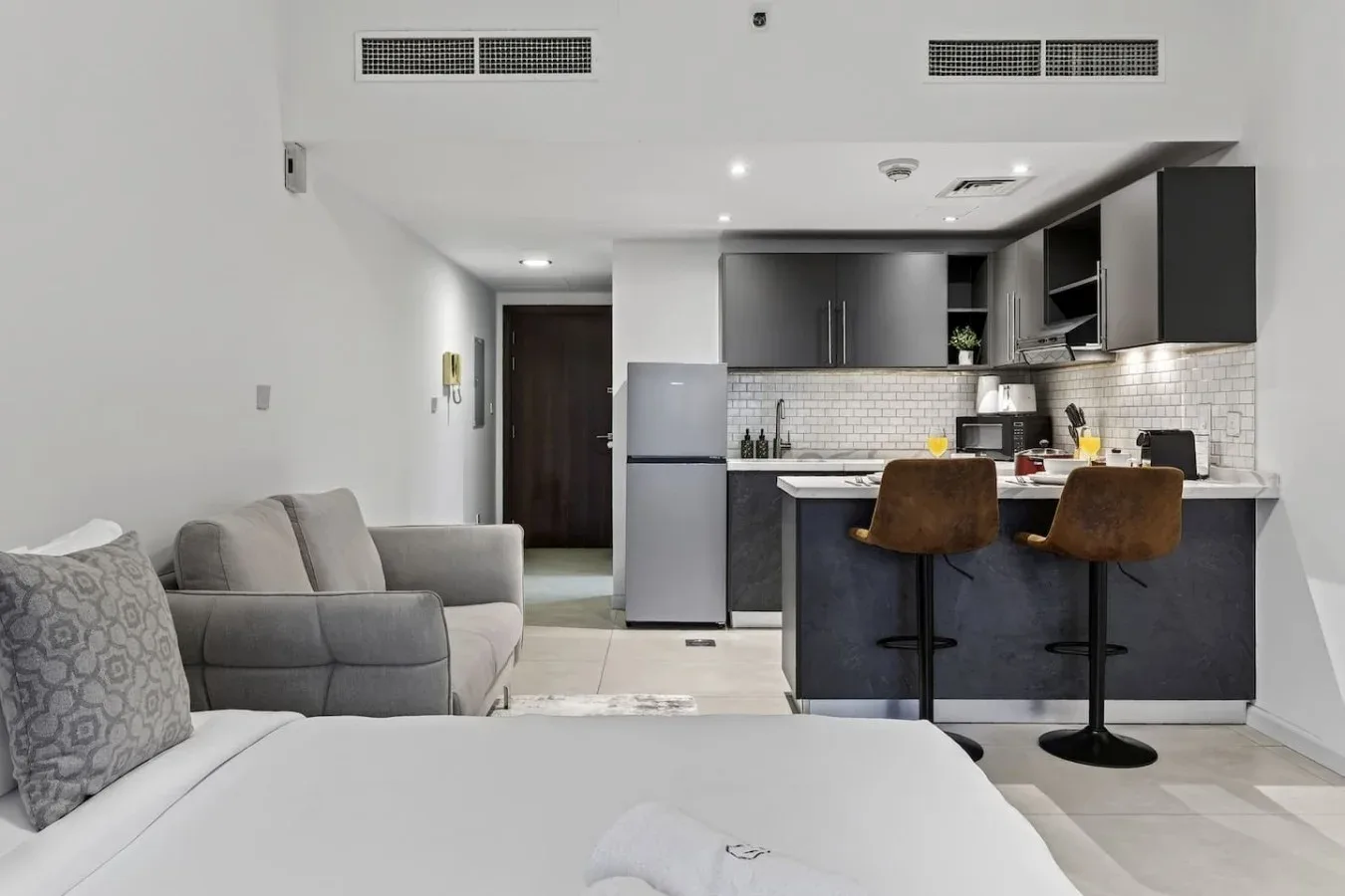Un dormitorio y una cocina abierta con cama, asientos y una barra para comer.
