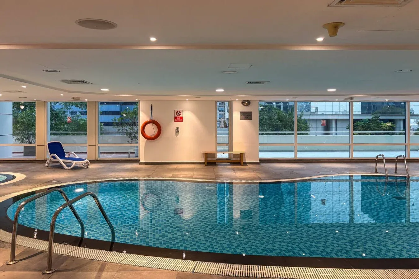 Una piscina cubierta con grandes ventanales y asientos de descanso a un lado.