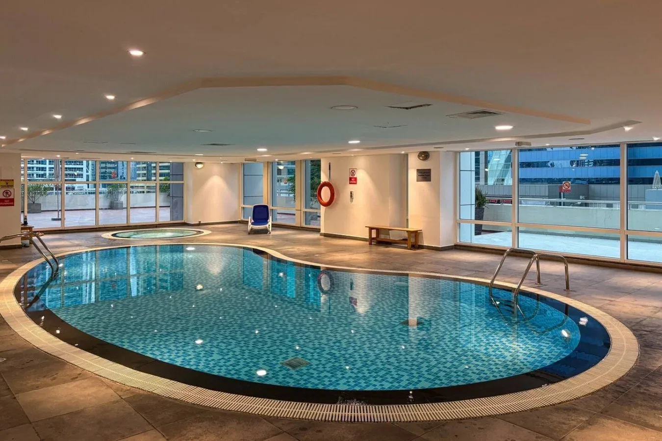 Una piscina cubierta con grandes ventanales y asientos junto al borde.