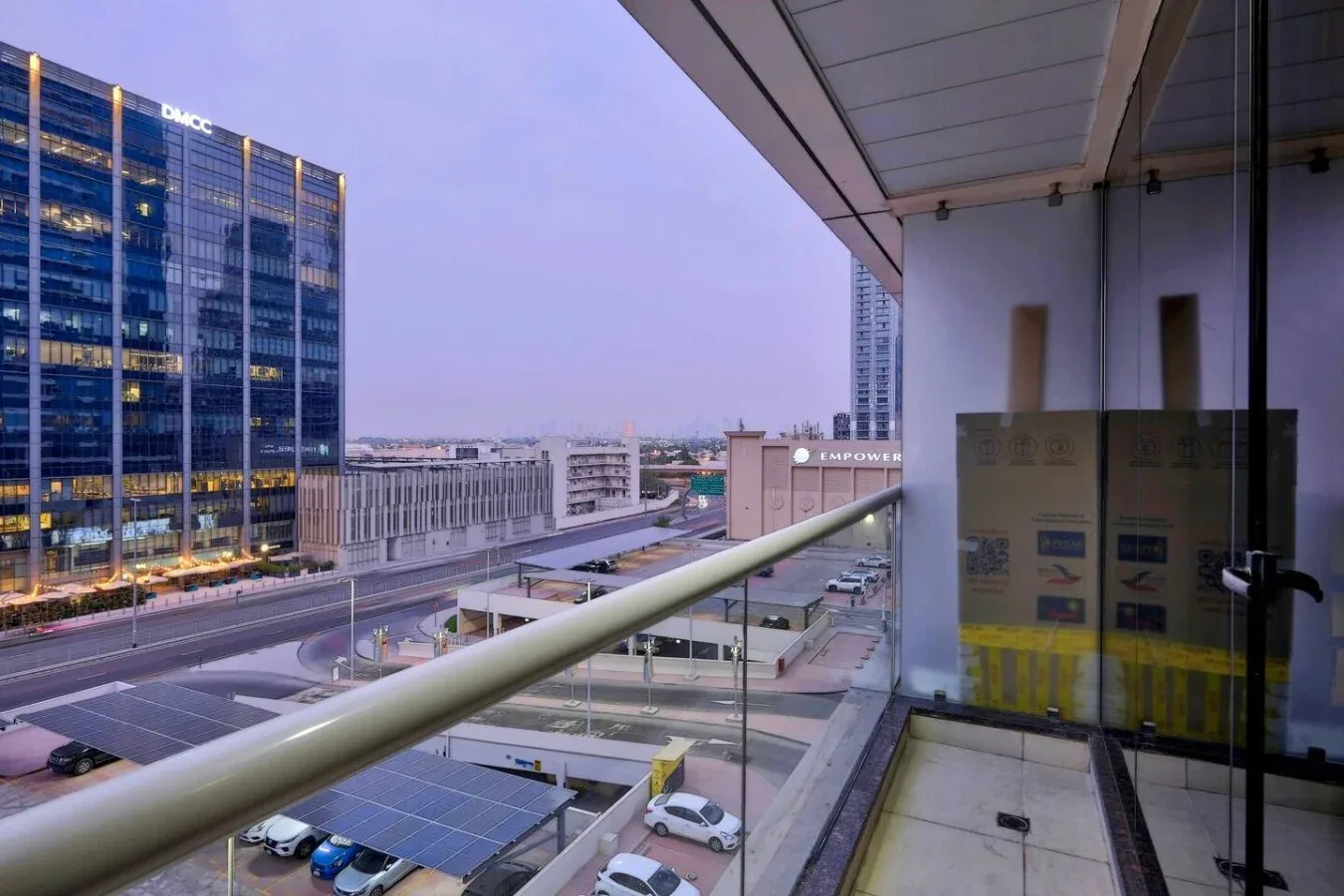 Un balcón da a edificios de oficinas cercanos y estacionamiento cubierto.