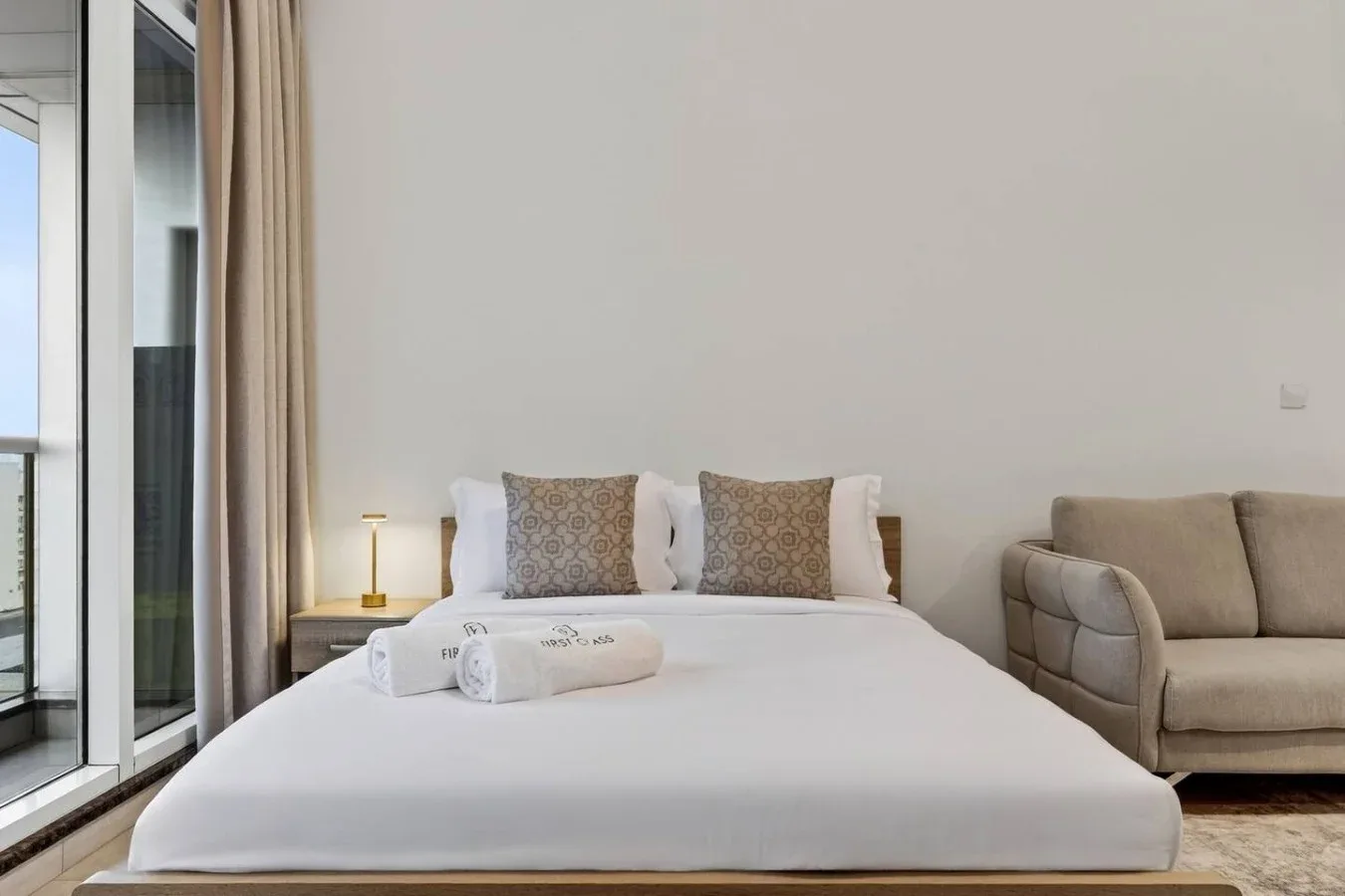 Un dormitorio luminoso con una cama bien tendida junto a una ventana grande.