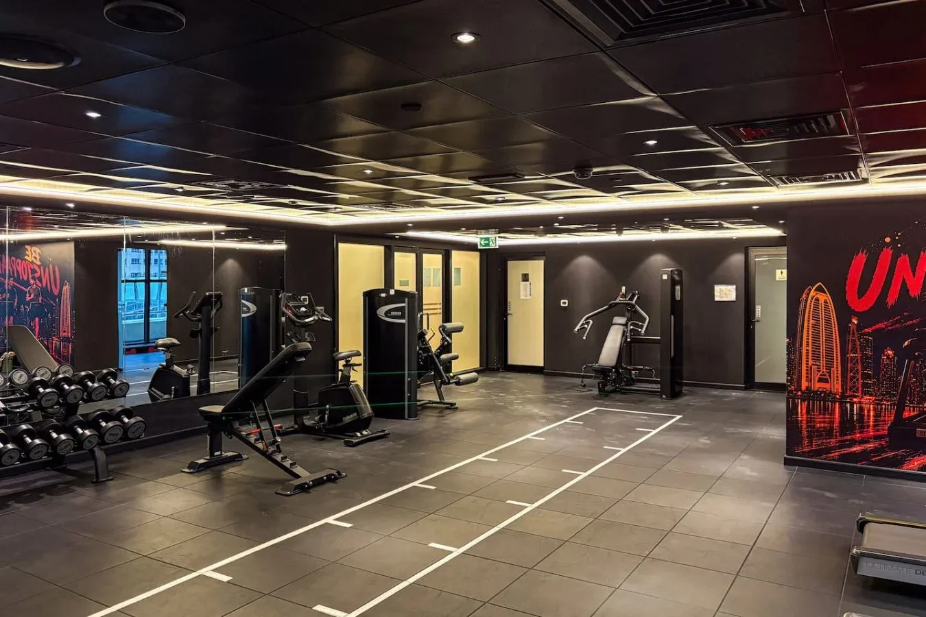 Un gimnasio con máquinas de ejercicio, mancuernas y carriles marcados.
