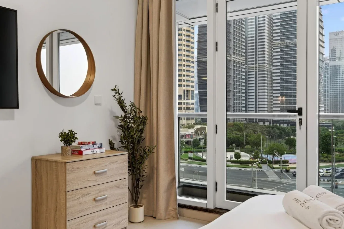 Un dormitorio con una cómoda y una ventana grande con vistas a edificios de la ciudad.