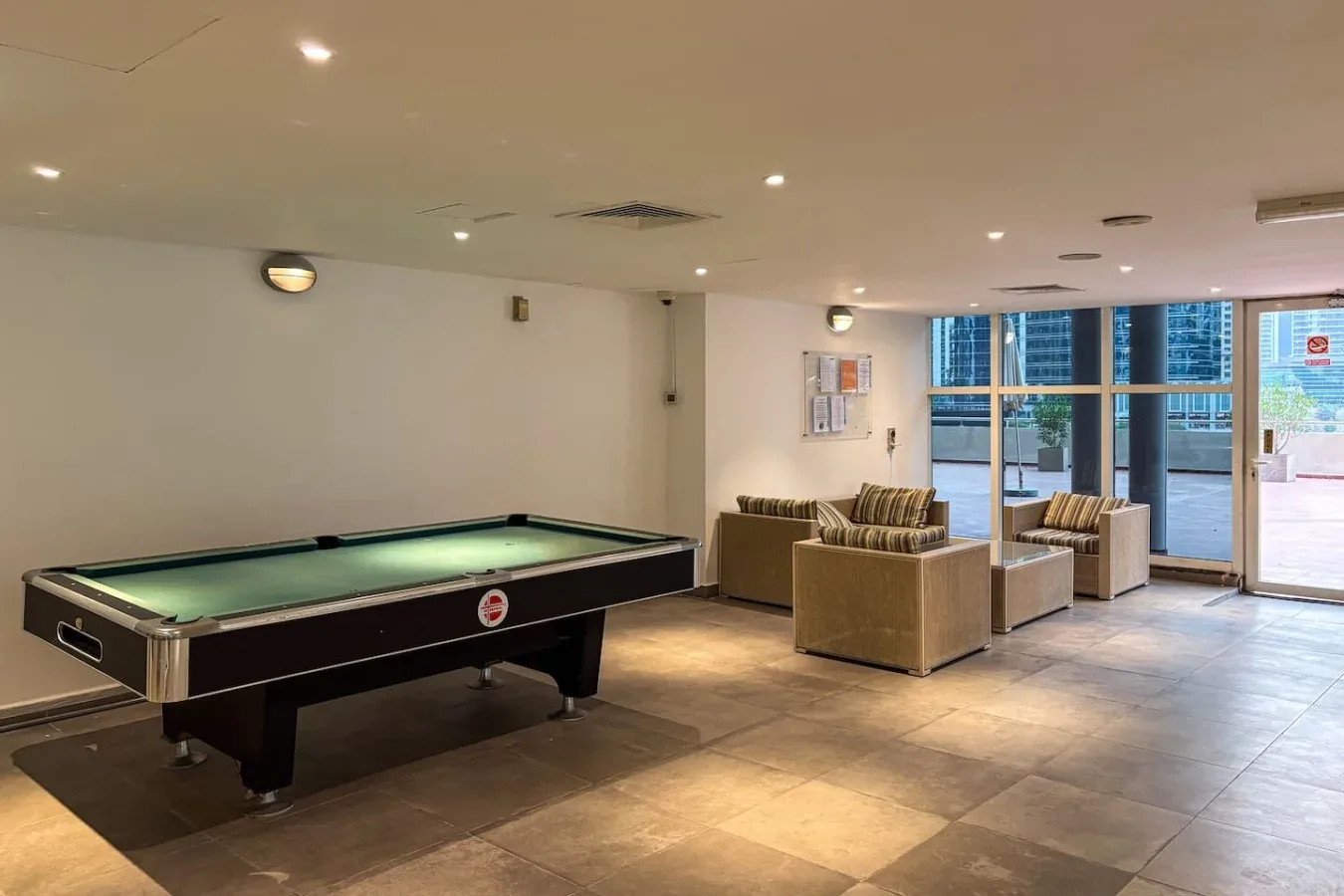 Sala de billar con una mesa de billar y asientos junto a grandes ventanas.
