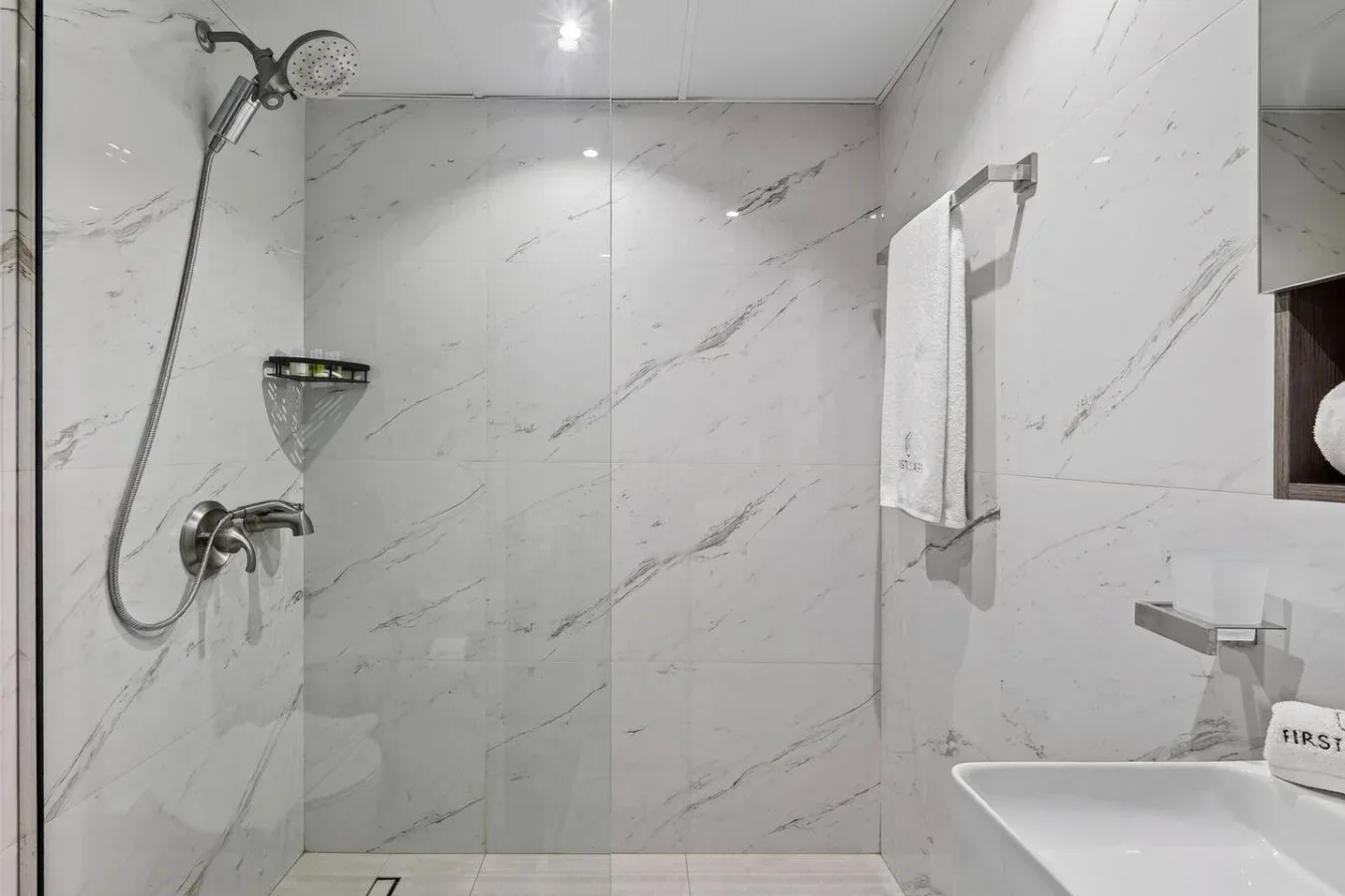 Zona de ducha con azulejos, ducha de mano y una toalla.