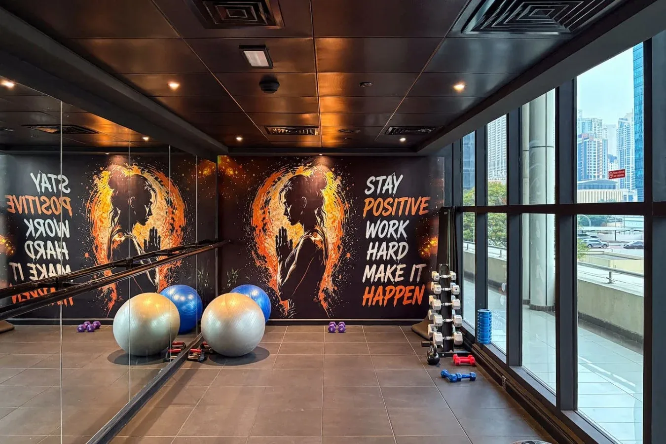 Una sala de ejercicio con balones y arte motivador en la pared, junto a grandes ventanas.