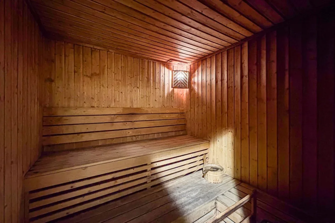Una sauna revestida de madera, con asientos escalonados y una pequeña luz en la pared.