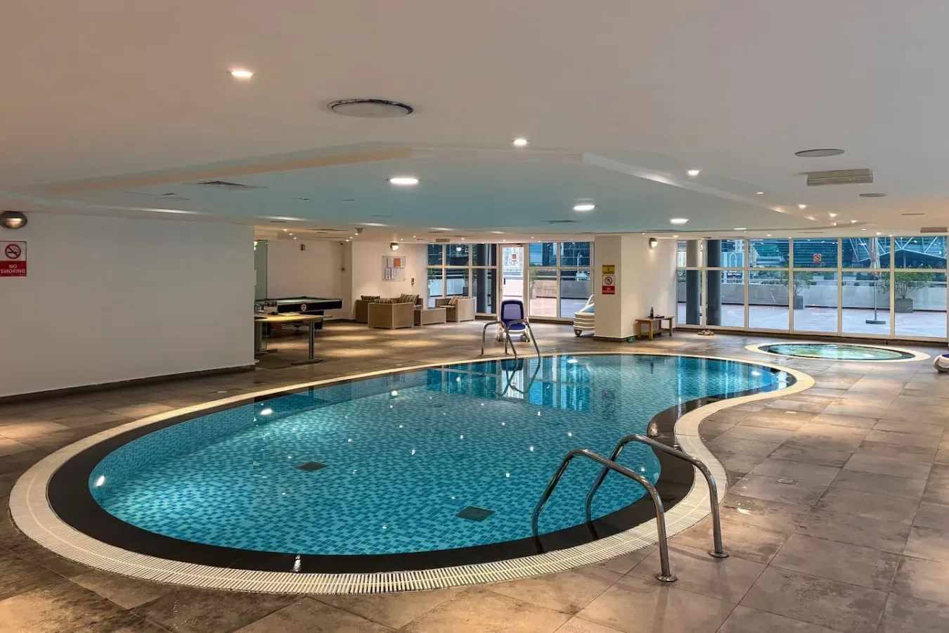 Una piscina cubierta con grandes ventanas y una zona de suelo embaldosado.