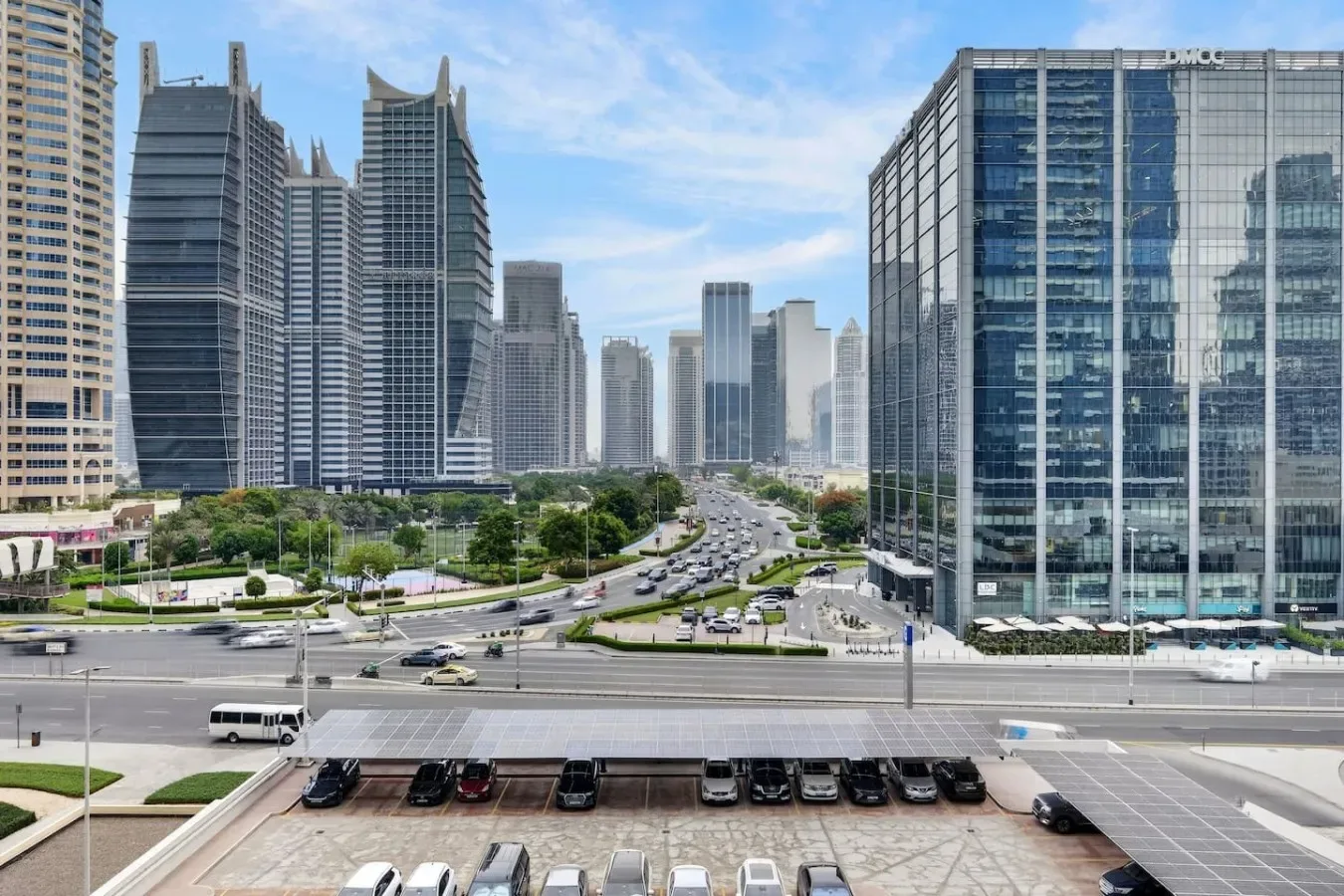 Una calle urbana se curva entre edificios modernos de gran altura bajo un cielo azul.