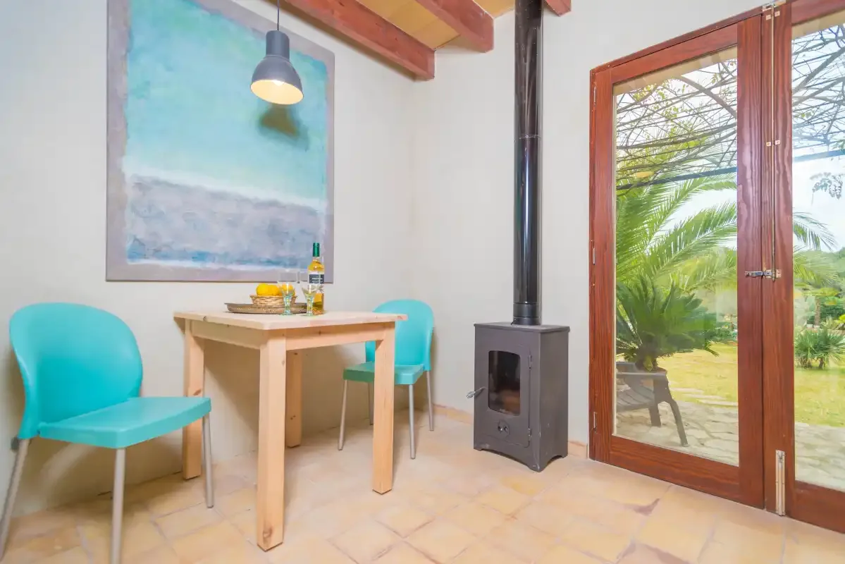 Comedor con una mesa de madera, asientos turquesa y puertas acristaladas que dan a la vegetación.
